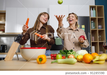 Mature mother and her adult daughter have fun while cooking in the kitchen Mature mother and her adult daughter have fun while cooking in the kitchen 91285590