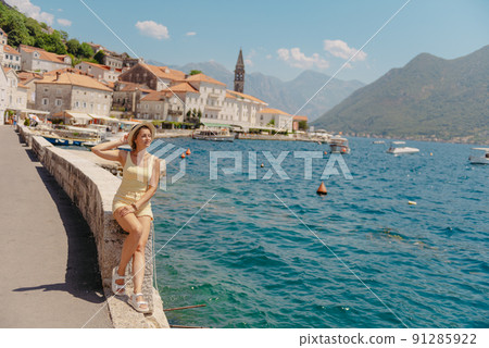 Summer photo shoot on the streets of Perast, Kotor, Montenegro. Beautiful girl in yellow dress and hat. smiling tourist girl with hat. Spectacular view of Montenegro with copy space. fashion outdoor 91285922