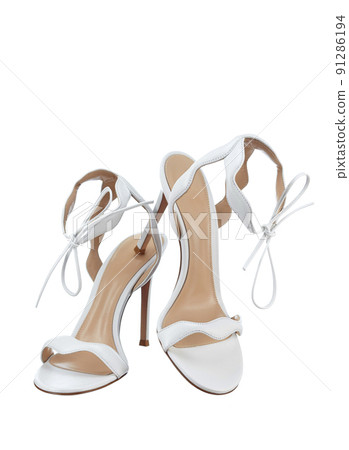 Pair of elegant women's open snow-white leather strappy sandals tied with a bow, with a high thin heel, isolated on a white background. The bride's shoes for the wedding ceremony. 91286194