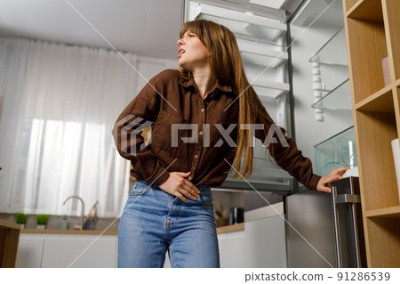 Young woman standing near empty refrigerator feels pain in her stomach. .Hungry girl near empty fridge 91286539