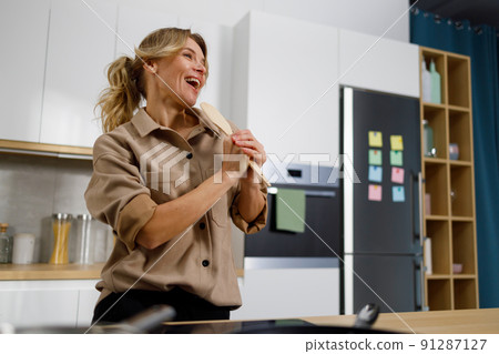 Happy housewife woman singing with a wooden spatula in the kitchen at home 91287127