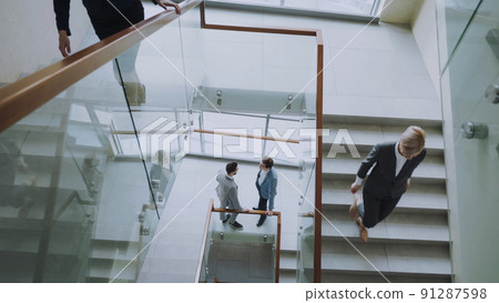 Top view of two businessmen meet at staircase in modern office center and talking while female colleagues walking stairs 91287598