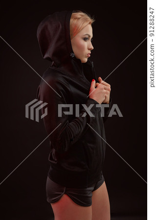 Beautiful seductive sporty girl with the slim sexy figure in the black hoodie, sport underwear and little black shorts is posing in the studio 91288247