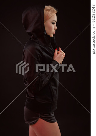 Beautiful seductive sporty girl with the slim sexy figure in the black hoodie, sport underwear and little black shorts is posing in the studio 91288248