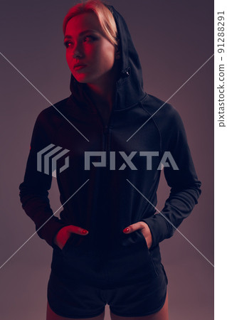 Beautiful seductive sporty girl with the slim sexy figure in the black hoodie, sport underwear and little black shorts is posing in the studio 91288291