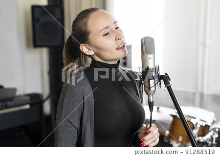 Young Asian or Caucasian woman singing to microphone in music or radio studio 91288319