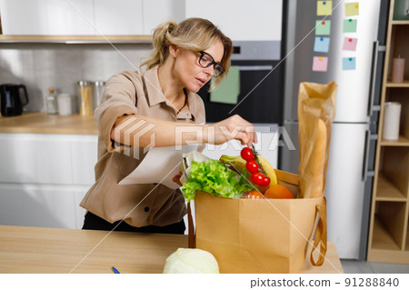 Attractive mature woman in kitchen holding shopping list looking through items Attractive mature woman in kitchen holding shopping list looking through items 91288840