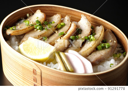 Photographed a grilled meat lunch box containing pickles, cut lemon and pork jowl in a bent wappa on a black background 91291778