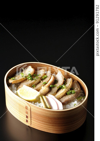 Photographed a grilled meat lunch box containing pickles, cut lemon and pork jowl in a bent wappa on a black background Photographed a grilled meat lunch box containing pickles, cut lemon and pork jowl in a bent wappa on a black background 91291782