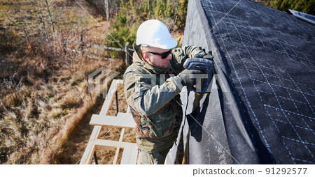 Male builder installing waterproof membrane on the wall of future cottage. Man worker building wooden frame house. Carpentry and construction concept. Male builder installing waterproof membrane on the wall of future cottage. Man worker building wooden frame house. Carpentry and construction concept. 91292577