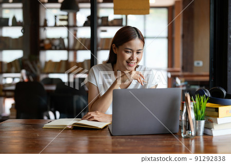 Pensive young asian woman in headphones work on laptop talk speak on video webcam call online. Smart ethnic female in earphones study distant on computer at home. Education concept. 91292838