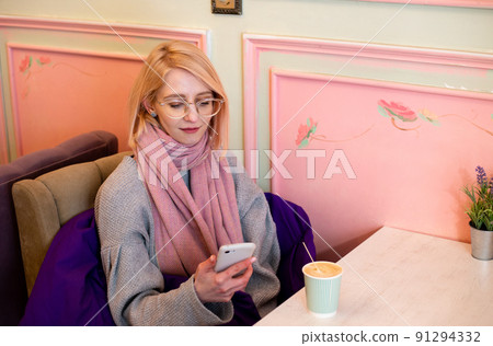 Young blonde woman in cafe drinks coffee and communicates on a smartphone Young blonde woman in cafe drinks coffee and communicates on a smartphone 91294332