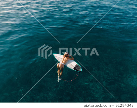 Sexy surfgirl relaxing on surfboard in transparent ocean. Aerial view 91294342