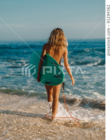 Naked surf woman with surfboard on beach goes... - Stock Photo