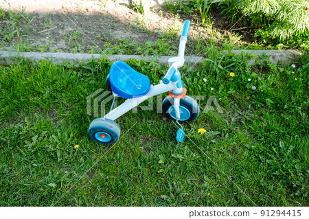 a plastic children's tricycle left in the yard on the lawn a plastic children's tricycle left in the yard on the lawn 91294415
