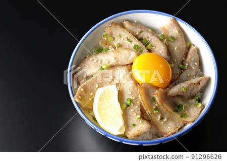 A bird's-eye view of a pork bowl with cut lemon and egg yolk and a grilled meat bowl on a black background 91296626