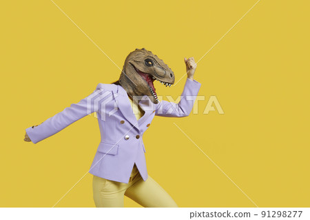 Crazy woman with with t-rex mask threatening someone with her fist, copy space for text on yellow background . Studio shot, portrait. Absurd and funny trend concept 91298277
