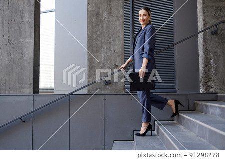 Portrait of elegant business woman in a suit walking down the stairs Portrait of elegant business woman in a suit walking down the stairs 91298278