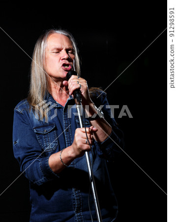 elderly man with long gray hair in blue denim shirt sings into a microphone on stage elderly man with long gray hair in blue denim shirt sings into a microphone on stage 91298591