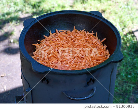 Cooking pilaf in a cauldron on fire in the garden. Carrot cut into thin slices 91300933