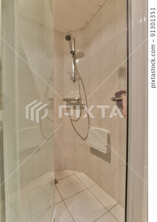 Flush toilet located between sink and shower in small tiled bathroom of contemporary apartment 91301351