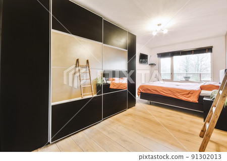 Comfortable bed located near glowing lamp and framed pictures in contemporary bedroom with small window and TV 91302013