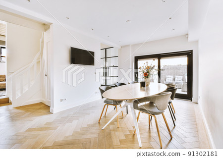 Table with chairs located under stylish plant near potted plants and framed picture against balcony door and windows in contemporary flat Table with chairs located under stylish plant near potted plants and framed picture against balcony door and windows in contemporary flat 91302181