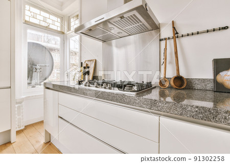 Modern minimalist style interior design of studio apartment with open white kitchen and dining zone with table and chairs illuminated by loft style lamp Modern minimalist style interior design of studio apartment with open white kitchen and dining zone with table and chairs illuminated by loft style lamp 91302258