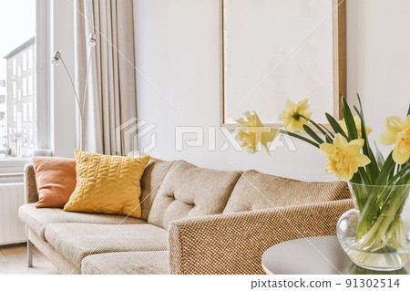 A comfortable sofa near the wall in a bright room next to a small table with a bouquet of yellow flowers in a vase 91302514