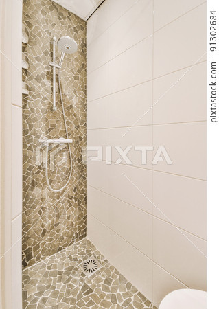 Shower faucets attached to tiled wall near glass partition and ornamental curtail in washroom at home 91302684