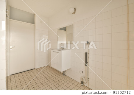 Cupboard with sink and mirror attached to tiled wall near door and drying rack in modern restroom 91302712