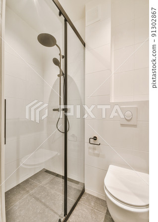 Shower faucets attached to tiled wall near glass partition and ornamental curtail in washroom at home Shower faucets attached to tiled wall near glass partition and ornamental curtail in washroom at home 91302867