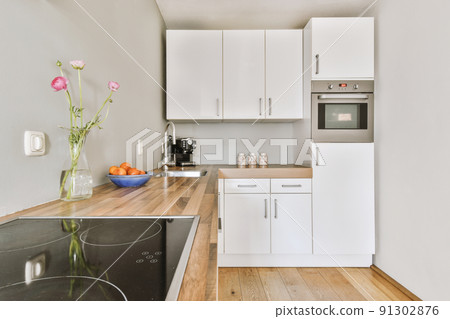 Modern home kitchen corner interior design with white cupboards and cabinets and steel hood over stove in contemporary apartment 91302876