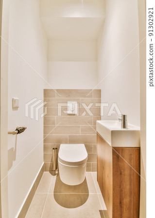 Modern flush toilet and ceramic sink installed on white tiled walls near mirror and towel in small restroom at home 91302921