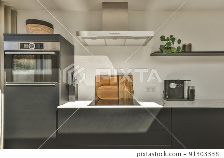 Interior of contemporary kitchen with stylish black cupboards and appliances near dining area in contemporary apartment Interior of contemporary kitchen with stylish black cupboards and appliances near dining area in contemporary apartment 91303338