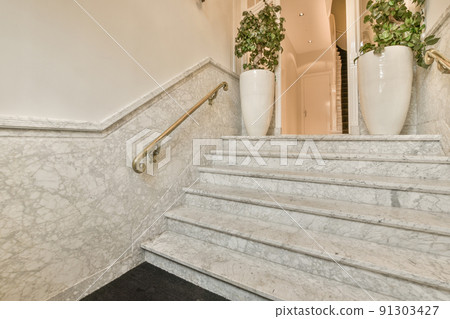 A spacious bright corridor with a marble staircase and an minimalistic plants A spacious bright corridor with a marble staircase and an minimalistic plants 91303427