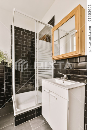 Bathtub with glass shower placed in corner near sink and mirror in small light bathroom with whiteand black tile walls Bathtub with glass shower placed in corner near sink and mirror in small light bathroom with whiteand black tile walls 91303601