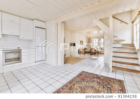 Table with chairs near lounge area and kitchen in spacious room of contemporary apartment Table with chairs near lounge area and kitchen in spacious room of contemporary apartment 91304238