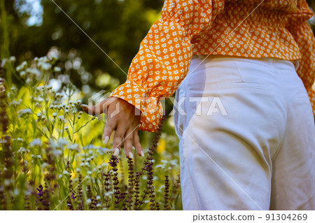 At one with nature. A girl enjoying summer sunny day. Young stylish happy woman walks through a field grass, blooming meadow touching flowers with hand. Summer vacation outdoor away from civilization. At one with nature. A girl enjoying summer sunny day. Young stylish happy woman walks through a field grass, blooming meadow touching flowers with hand. Summer vacation outdoor away from civilization. 91304269