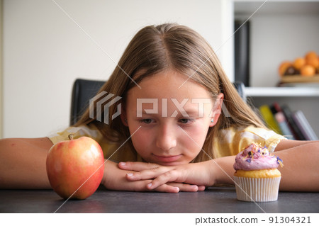 the girl chooses between a cupcake and an apple 91304321