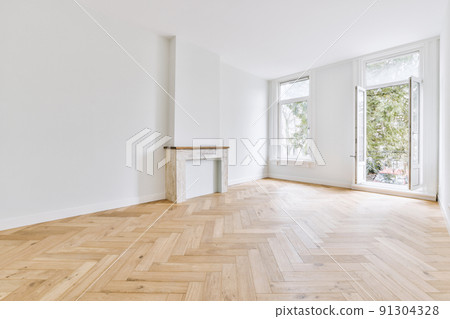 Interior of spacious light room with fireplace and elegant chandelier against balcony door and windows 91304328