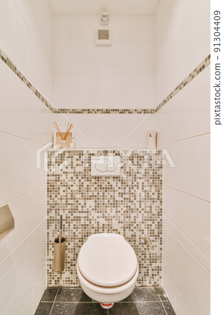 A modern toilet is installed on the wall under a button and a shelf with a diffuser in a light restroom at home 91304409