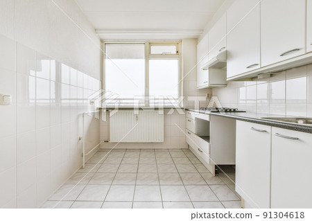 Fragment of interior of light narrow home kitchen with minimalist style white furniture with sink and stove Fragment of interior of light narrow home kitchen with minimalist style white furniture with sink and stove 91304618