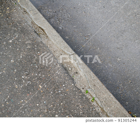 Destroyed curb stone on the sidewalk by the road 91305244