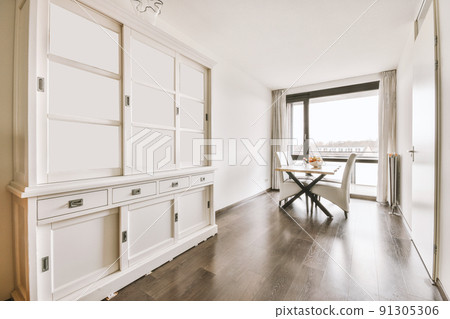 Large white wooden cupboard in the empty room with a set of chairs and dining table Large white wooden cupboard in the empty room with a set of chairs and dining table 91305306