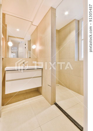 Cupboard with sink and mirror attached to tiled wall near door and drying rack in modern restroom Cupboard with sink and mirror attached to tiled wall near door and drying rack in modern restroom 91305487