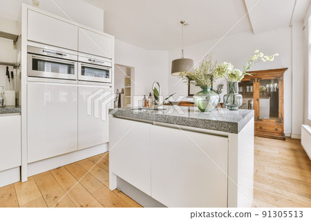 Modern minimalist style interior design of studio apartment with open white kitchen and dining zone with table and chairs illuminated by loft style lamp 91305513