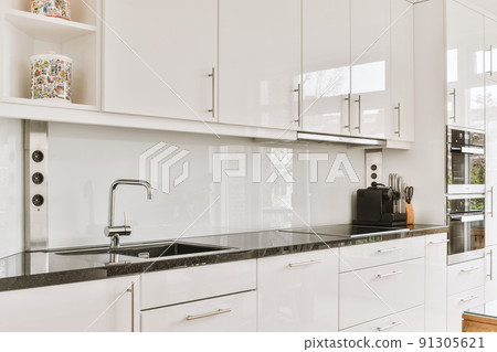 Fragment of interior of light narrow home kitchen with minimalist style white furniture with sink and stove Fragment of interior of light narrow home kitchen with minimalist style white furniture with sink and stove 91305621