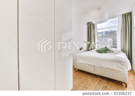 Comfortable bed and wardrobe placed in small narrow minimalist style bedroom with white walls and green curtains on window in modern apartment Comfortable bed and wardrobe placed in small narrow minimalist style bedroom with white walls and green curtains on window in modern apartment 91306237