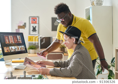 Retoucher examining photos together with photo editor before retouching them on computer 91306326